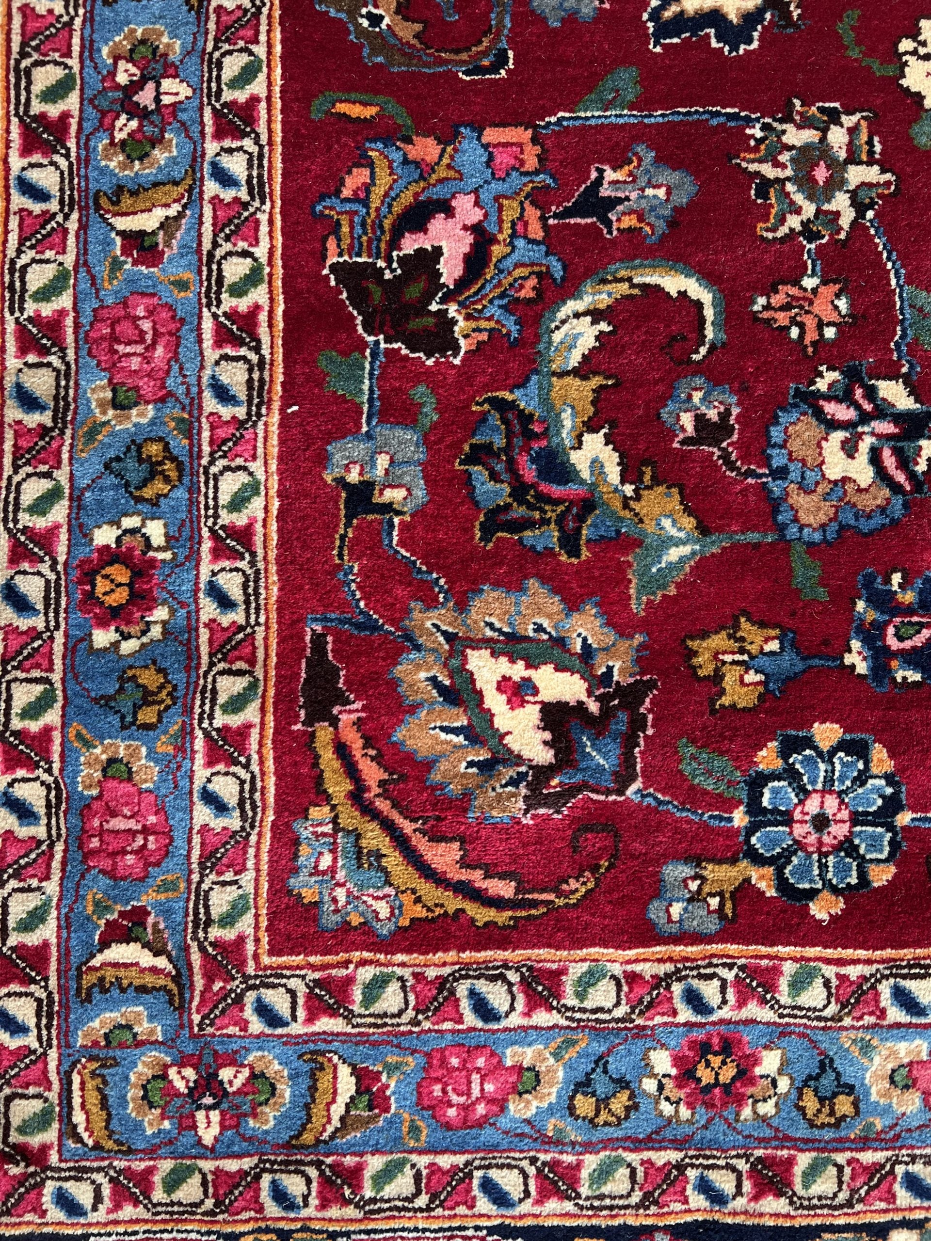 Antique hand-knotted Persian Mashad wool rug corner with thick, luxurious pile.  Rich ruby red ground and deep cornflower blue border with intricate floral and vine motifs.