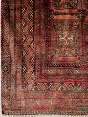 Vintage Turkoman wool area rug corner close up with geometric patterns and motfis in faded shades of rust red, charcoal and dark brown.
