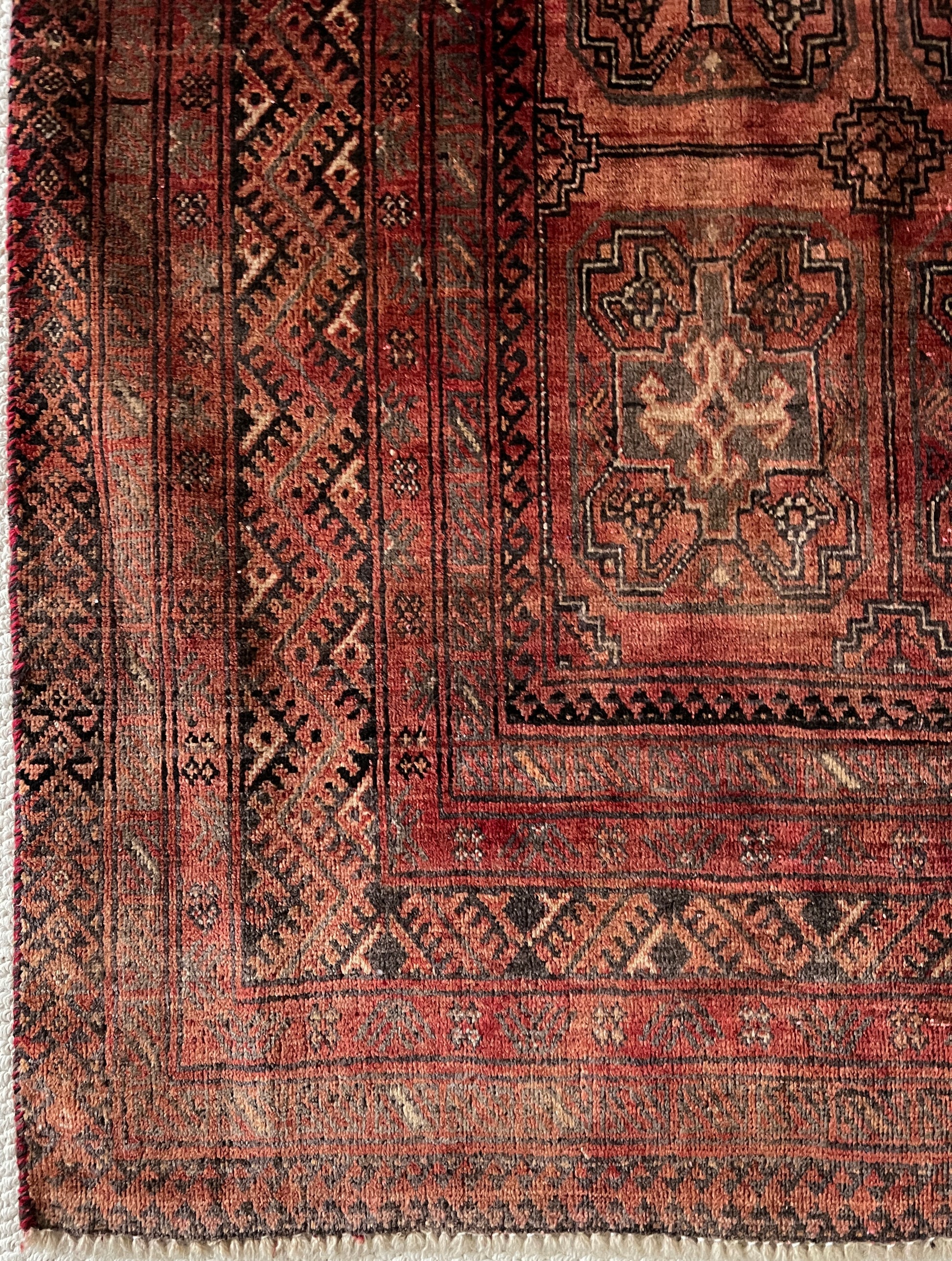 Vintage Turkoman wool area rug corner close up with geometric patterns and motfis in faded shades of rust red, charcoal and dark brown.