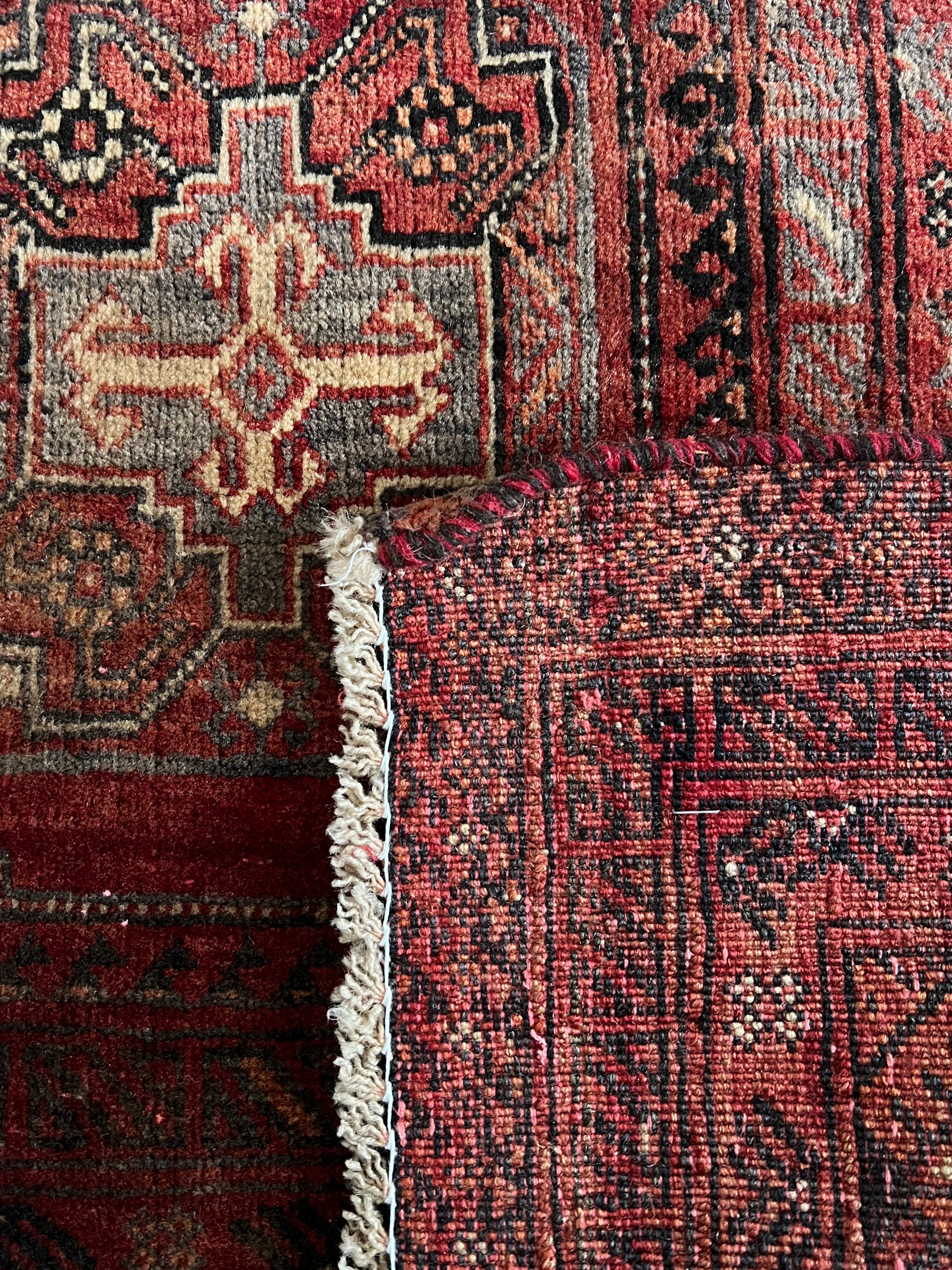 Vintage Persian wool area rug detail of rug back to show knotting. Geometric pattern in red with cream, charcoal and dark brown accents.