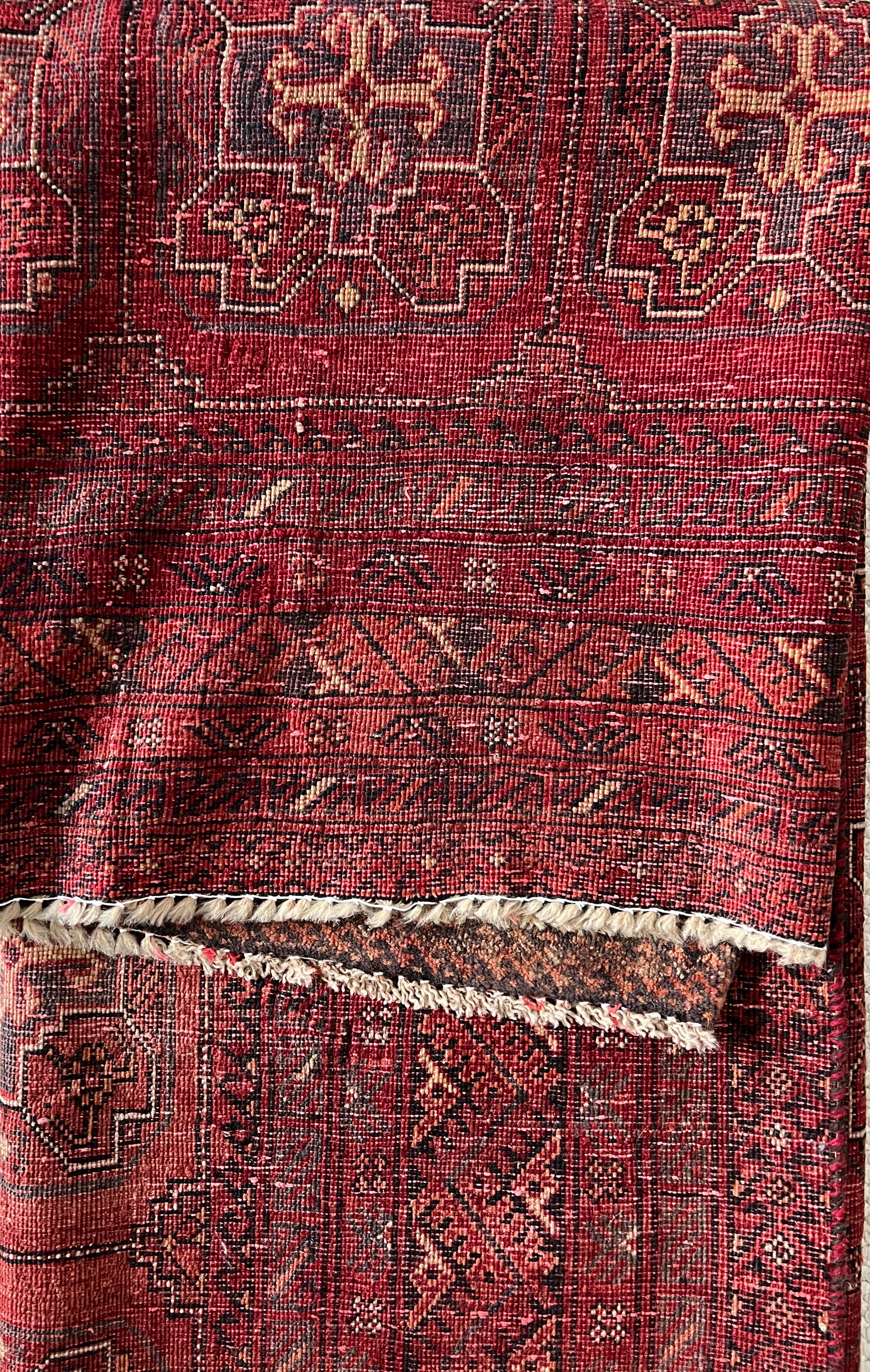 Vintage Persian wool area rug back to show knotting detail and fringe.  Red with varying shades of red and rust in a geometric pattern with cream, charcoal and dark brown accents.