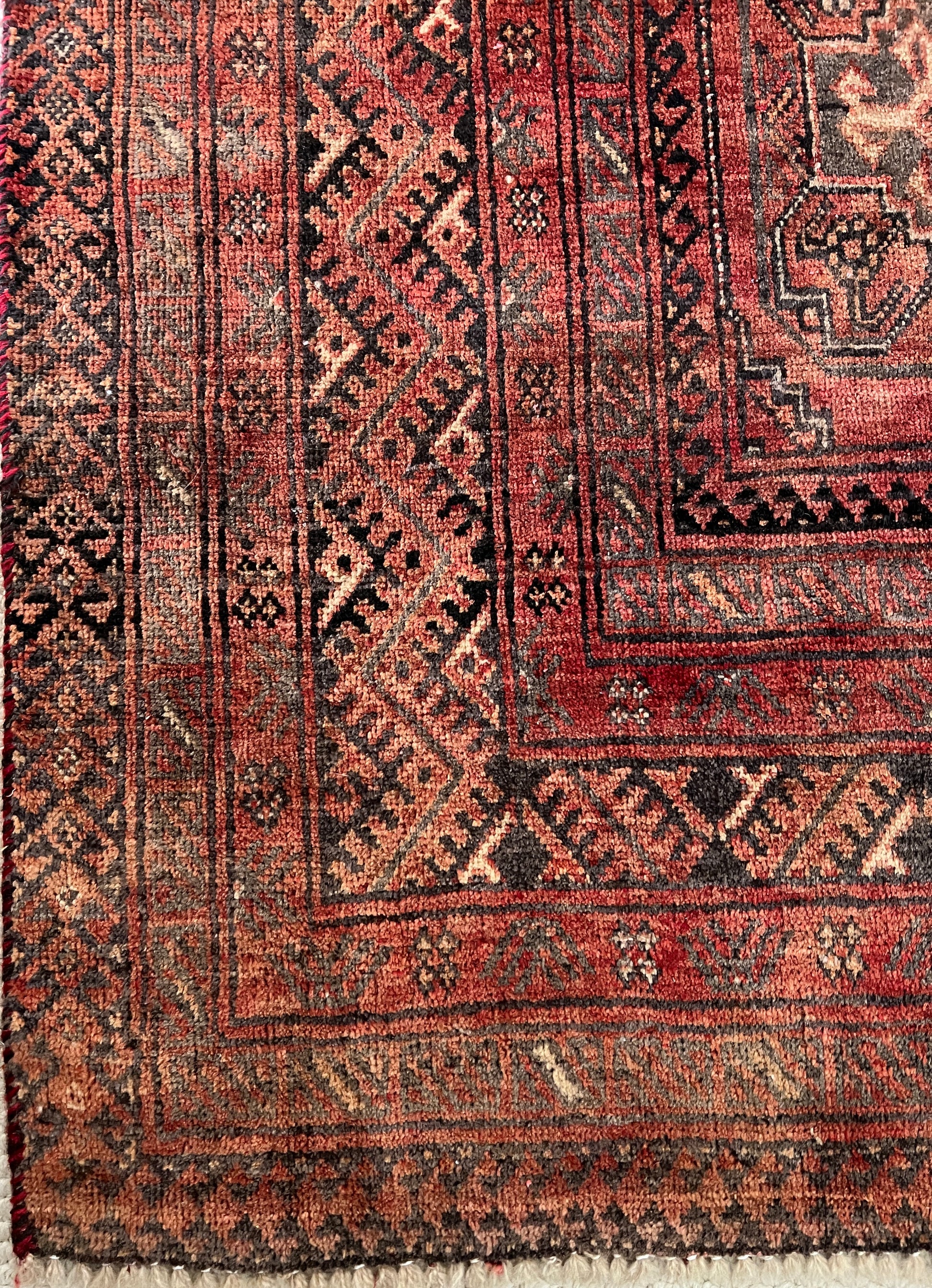 Vintage Persian wool area rug corner border detail with varying shades of red and rust in a geometric pattern with cream, charcoal and dark brown accents.