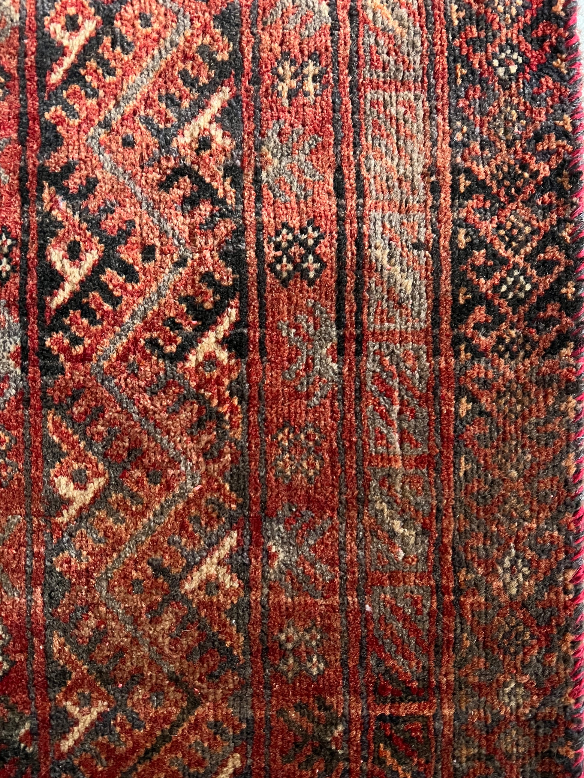 Vintage Persian wool area rug close up with varying shades of red and rust in a geometric pattern with cream, charcoal and dark brown accents to show abrash.