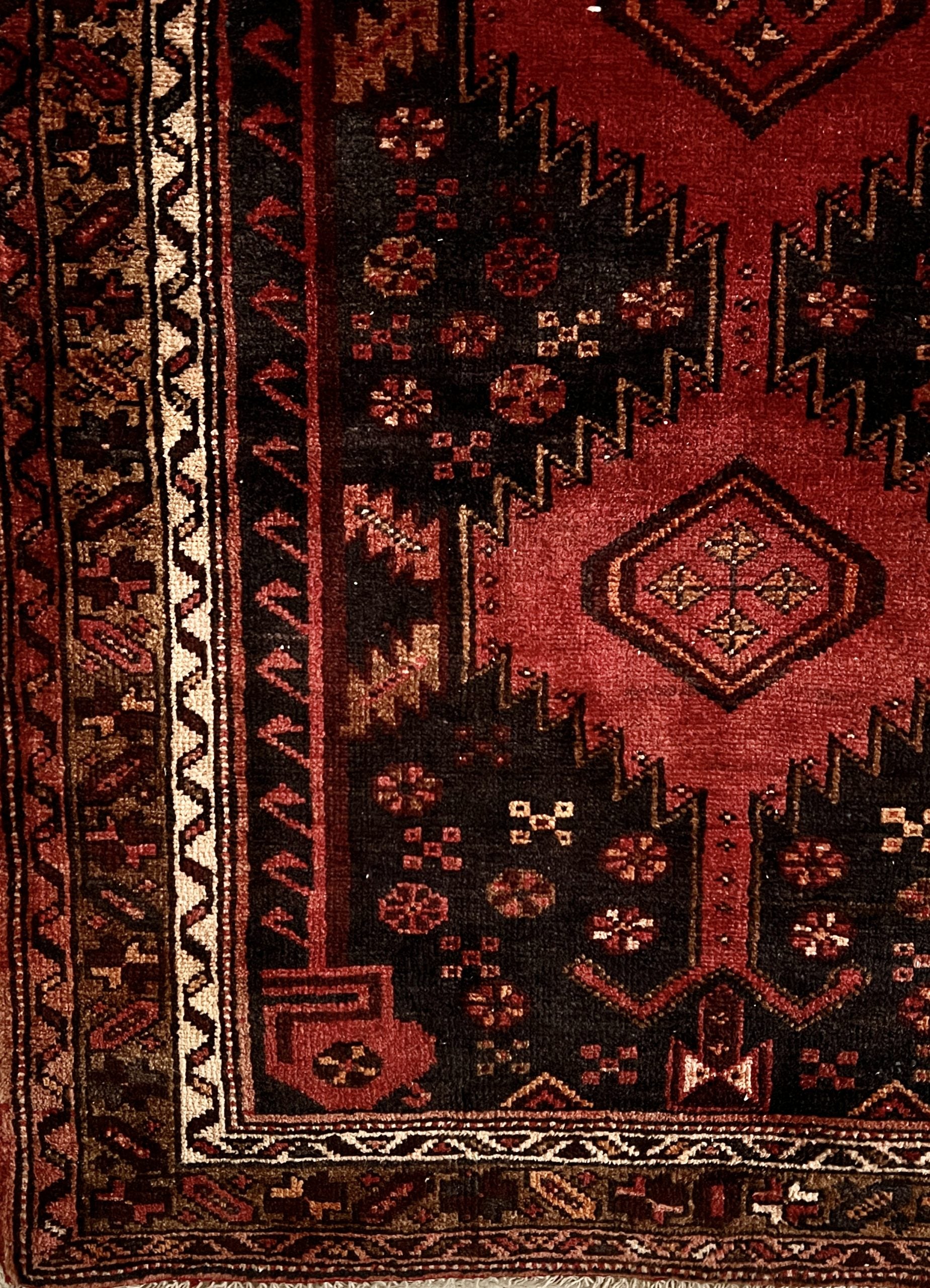 Vintage Persian tribal Heriz hand-knotted wool runner, 3x10. corner detail of geometric patterns in shades of red, dark brown and a geometric decorative border in brown, rust and cream.