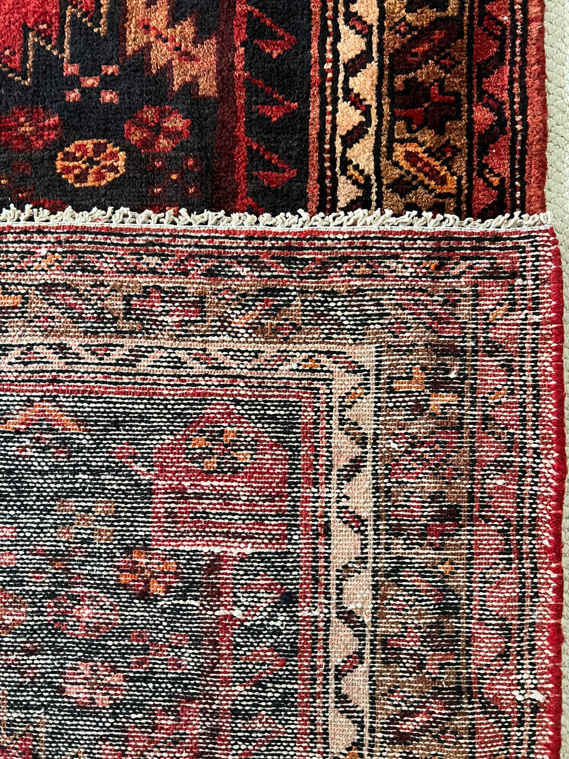 vintgae tribal heriz runner back detail to show hand knotting and fringe. Rug front detail shows black ground with fragment of geometric patterned border in shades of brown, cream and red.