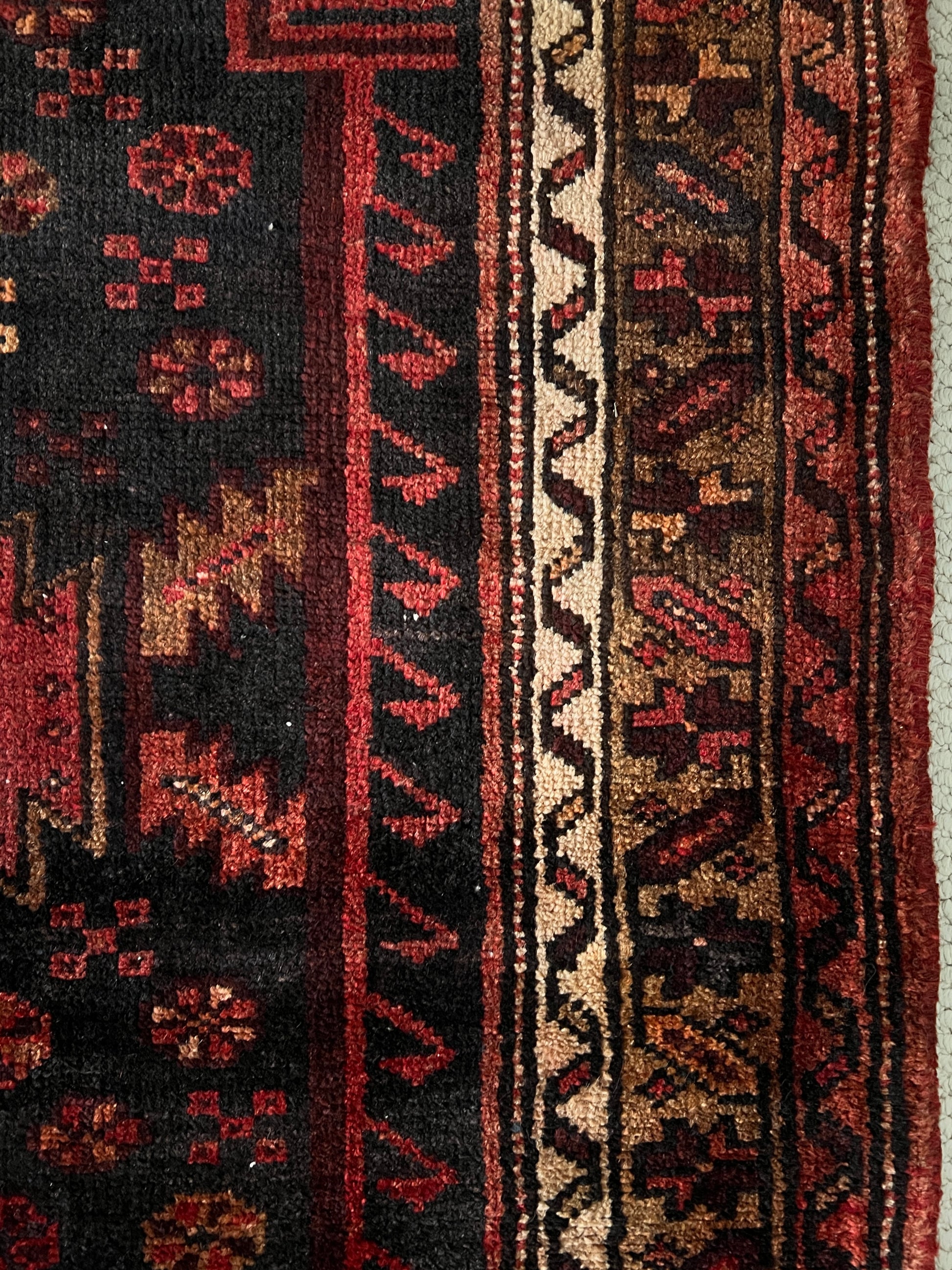 vintage heriz wool runner detail of border with intricate geometric patterns in shades of red and black with red, brown and cream accents.