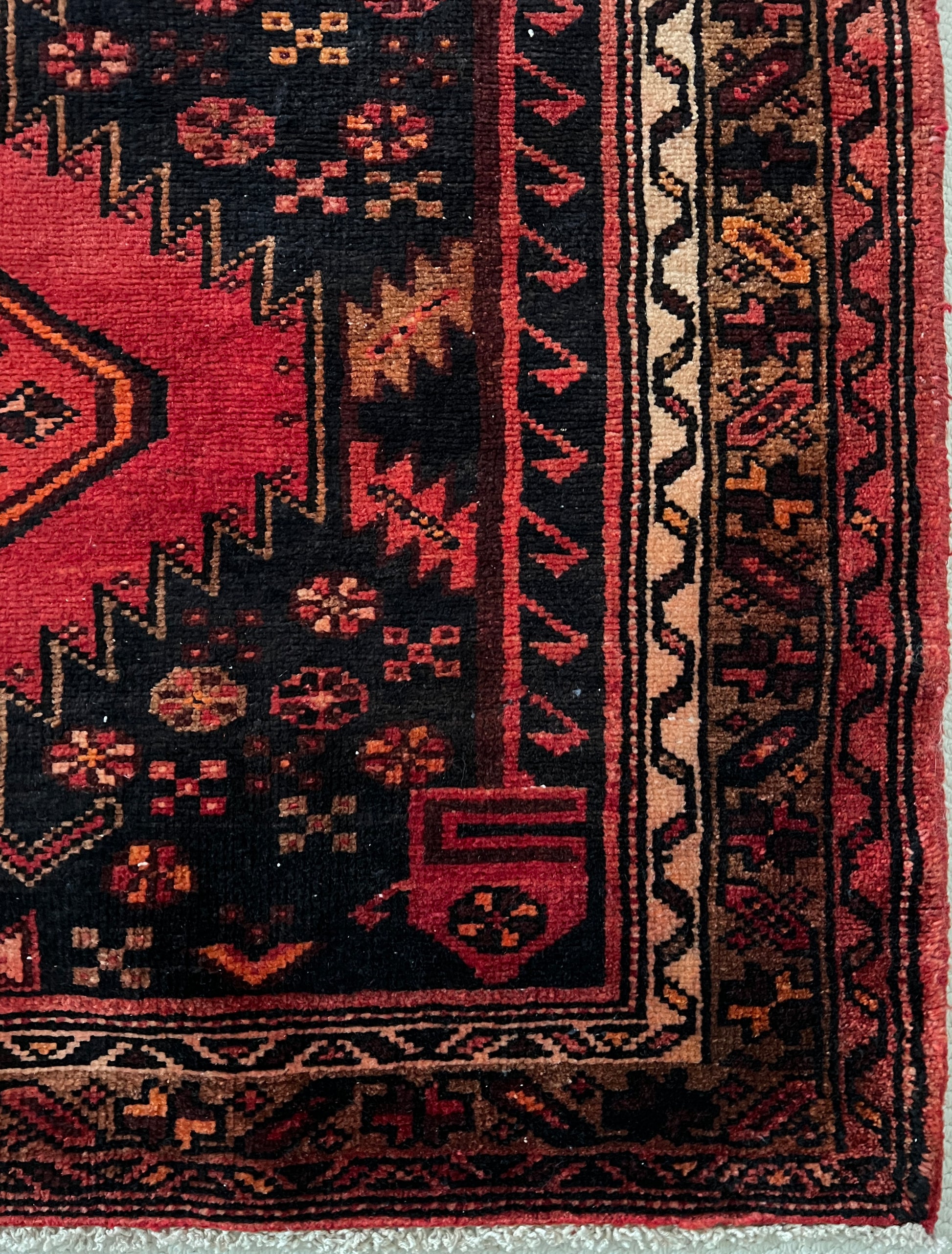vintage heriz runner detail of corner border with shades of red, black and cream and red details in a geometric pattern.