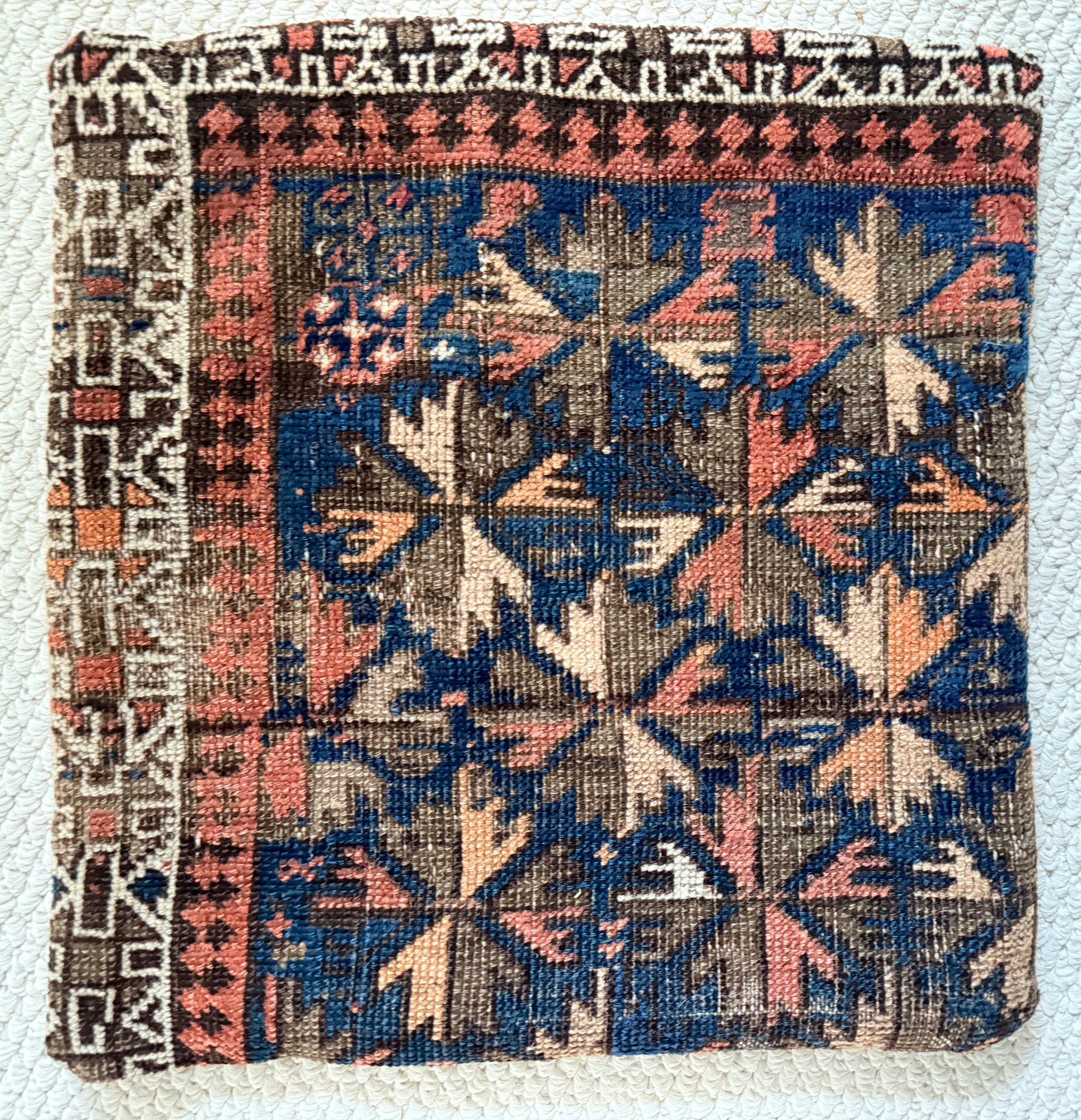 vintage Caucasian rug pillow with blue background and shades of coral, brown and cream in a geometric pattern.