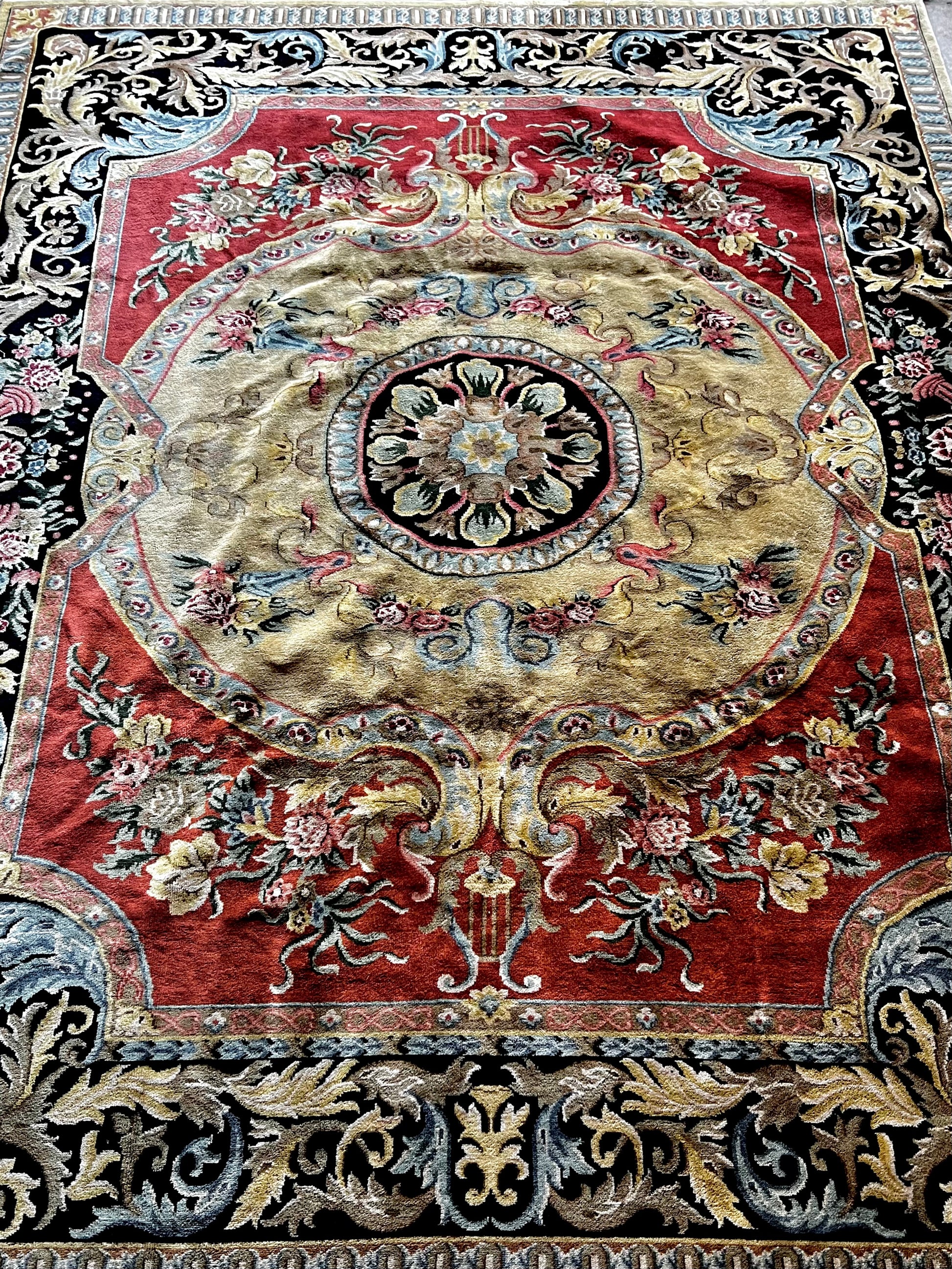 Vintage Indo-Aubusson large wool rug, hand-knotted in India, features a deep coral red ground with a large gold center medallion and a black border dotted with pale blue, pale pink, and very pale shades of buttery gold.