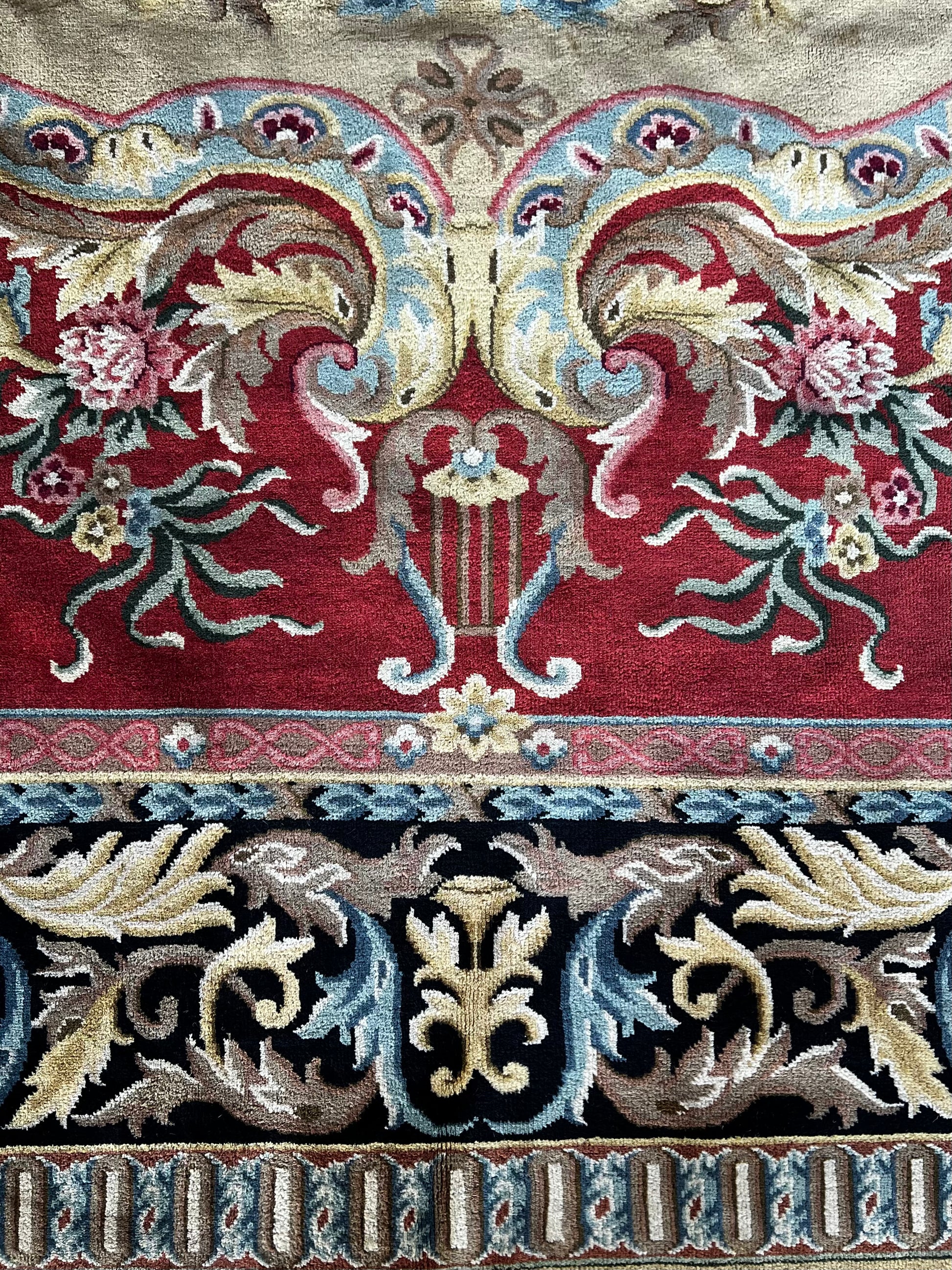 Vintage Indo-Aubusson large wool rug, hand-knotted in India, close look at detail featuring flowers, ribbon and a lyre. against a deep coral red and a black border dotted with pale blue, pale pink, and very pale shades of buttery gold.