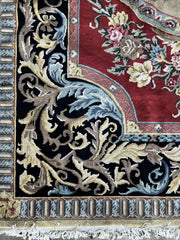 Vintage Indo-Aubusson large wool rug, hand-knotted in India, corner detail of a black border dotted with pale blue, pale pink, and very pale shades of buttery gold against a red ground.