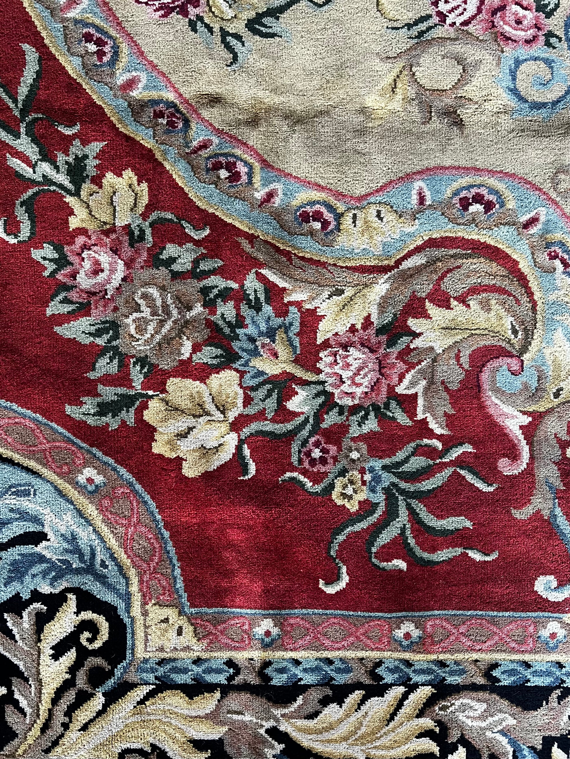 Vintage Indo-Aubusson style large wool rug, hand-knotted in India. Detail of flowers and ribbons against a deep coral red with pale blue, pale pink, and very pale shades of buttery gold.